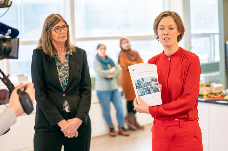 Wenche Halsen og Anette Trettebergstuen står ved siden av hverandre. Trettebergstuen holder opp en papirversjon av rapporten.