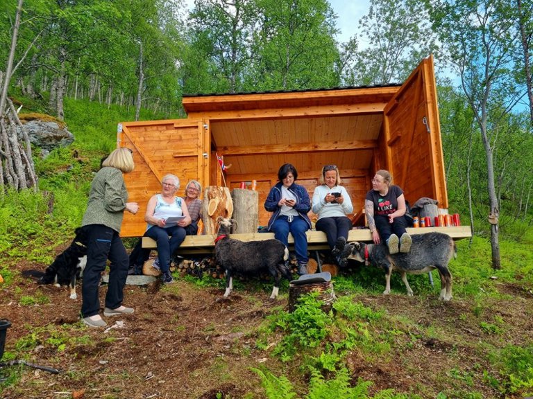 Flere mennesker, eldre og voksne sitter i en gapahuk.