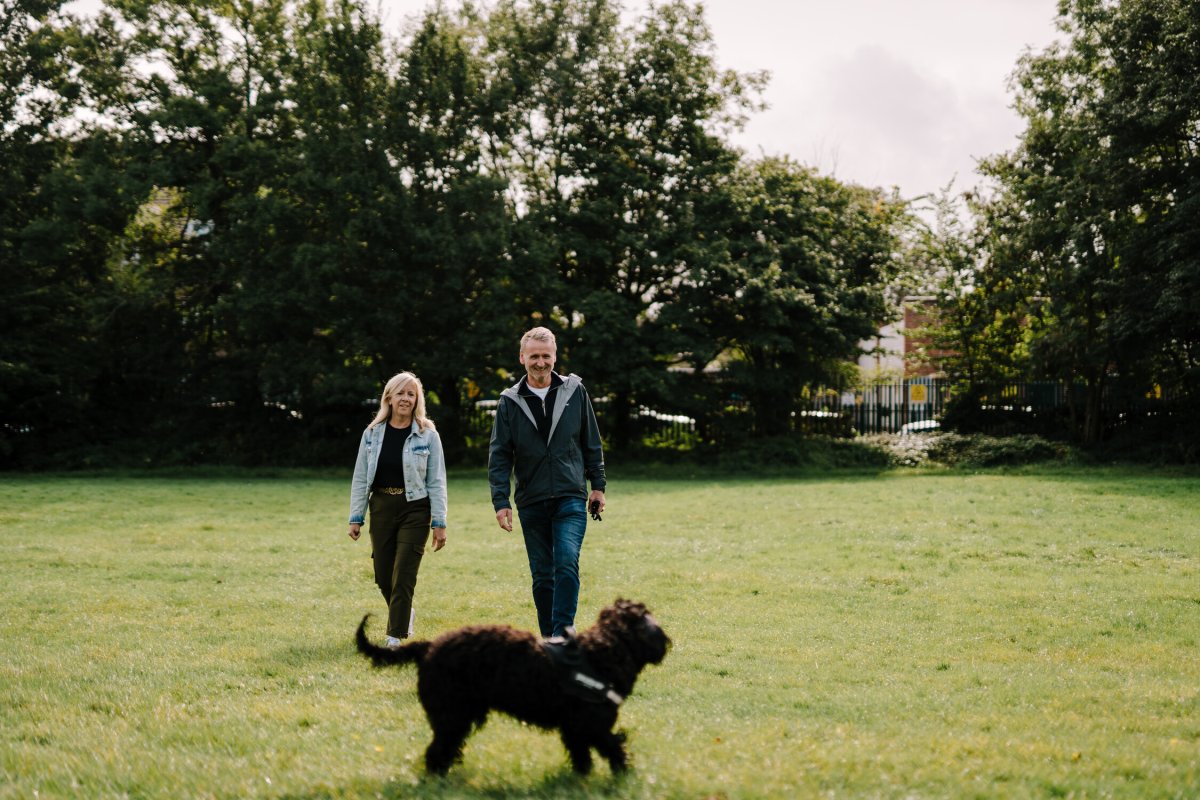 To personer går tur i en park og lufter en hund. 