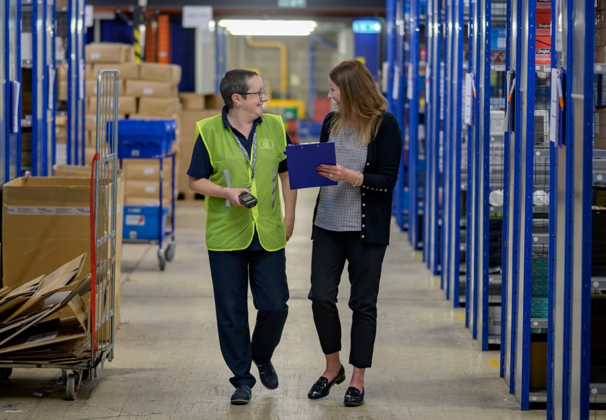 To damer går i midten av noen store reoler i en lagerbygning