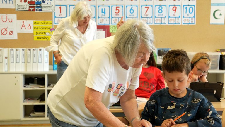 Eldre dame hjelper et barn i klasserommet