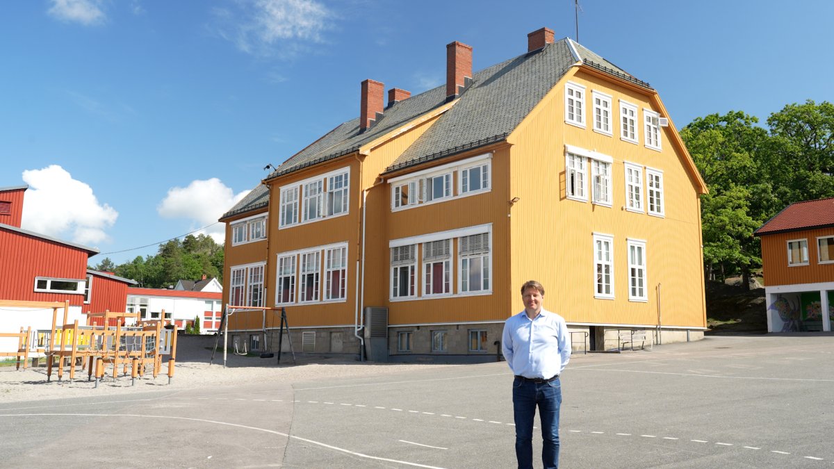 Rektor står utenfor en stor, eldre gul skolebygning