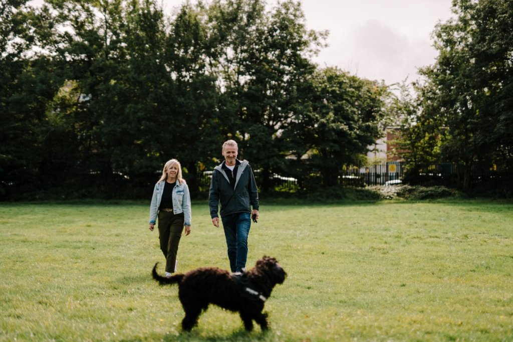 To voksne mennesker går i en park og lufter en hund