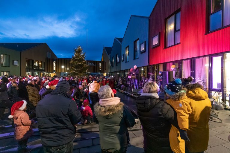 mennesker samles rundt et juletre ute foran hus